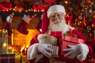 Noel Baba hediye kutusuyla şömine ve Noel ağacının yanında duruyor. Ahşap evin içindeki şenlikli iç mekan, Noel 'in neşeli ruhu. Gerçek beyaz sakallı son sınıf öğrencisi Noel Baba kostümü giyiyor..