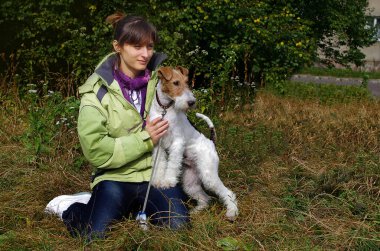 Genç bir kadın evcil hayvanıyla çimlerin üzerinde oturuyor. Kız köpek telli tilki teriyerini okşuyor..