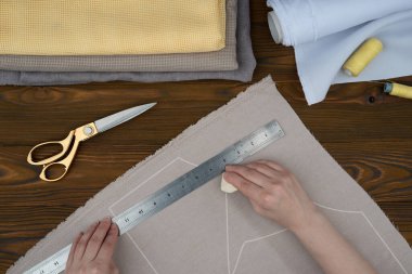 Kadın eli, kıyafet yapıyor. Özel dikim giysiler kes ve diktir. Makas, dikiş aksesuarları, ahşap masadaki kumaşlar..