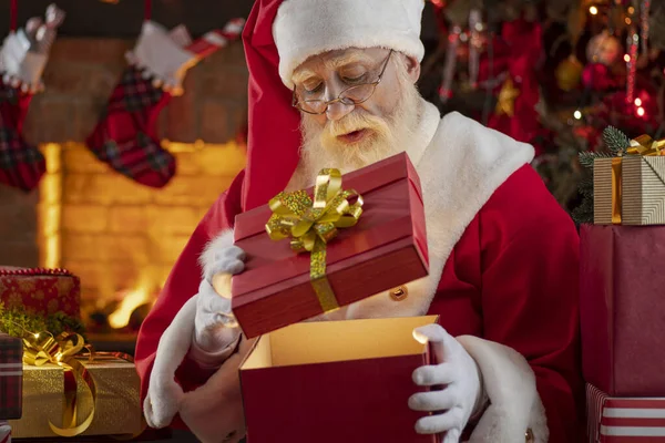 圣诞老人带着礼品盒在壁炉和圣诞树旁送礼 木屋内喜庆的室内空气 新年喜庆的气氛 圣诞的精神 长得象真的白胡子的老人 圣诞老人 — 图库照片