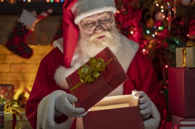 Noel Baba hediye kutusuyla şömine ve Noel ağacının yanında duruyor. Ahşap evin içindeki şenlikli iç mekan, Noel 'in neşeli ruhu. Gerçek beyaz sakallı son sınıf öğrencisi Noel Baba kostümü giyiyor..