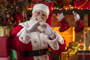 Noel Baba, elleri şöminenin ve Noel ağacının yanında kalp şekli veriyor. Ahşap evin içindeki şenlikli iç mekan, Noel 'in neşeli ruhu. Gerçek beyaz sakallı son sınıf öğrencisi Noel Baba kostümü giyiyor..