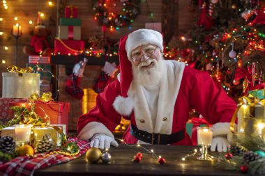 Noel Baba şöminenin ve Noel ağacının yanında. Ahşap evin içindeki şenlikli iç mekan, Noel 'in neşeli ruhu. Gerçek beyaz sakallı son sınıf öğrencisi Noel Baba kostümü giyiyor..