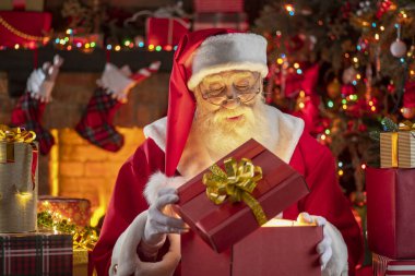 Noel Baba hediye kutusuyla şömine ve Noel ağacının yanında duruyor. Ahşap evin içindeki şenlikli iç mekan, Noel 'in neşeli ruhu. Gerçek beyaz sakallı son sınıf öğrencisi Noel Baba kostümü giyiyor..