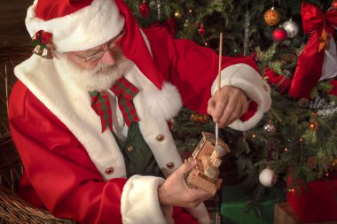 Noel Baba atölyede oyuncaklar yapıyor. Ahşap evin içindeki şenlikli iç mekanda. Yeni yılın neşeli Noel Ruhu. Gerçek beyaz sakallı son sınıf öğrencisi Noel Baba kostümü giyiyor..