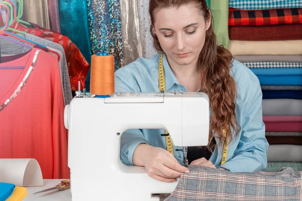 Creative female fashion designer tailoring clothes on a sewing machine, she has a measuring tape Lifestyle scene in a sewing Studio. Woman tailor creates fashionable dresses art