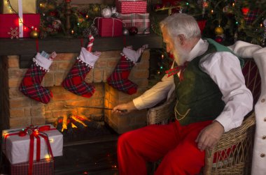 Noel Baba şöminenin ve Noel ağacının yanında. Ahşap evin içindeki şenlikli iç mekan, Noel 'in neşeli ruhu. Gerçek beyaz sakallı son sınıf öğrencisi Noel Baba kostümü giyiyor..