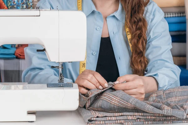 Creative female fashion designer tailoring clothes, she has a measuring tape Sewing machine in a desk. Lifestyle scene in a sewing Studio. Woman tailor creates needlework fashionable dresses art