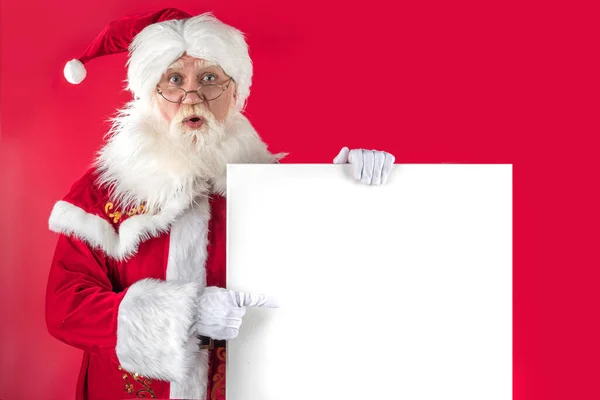 Noel Baba Kırmızı Arka Planda Beyaz Tahtayı Göstererek Işaret Ediyor — Stok fotoğraf