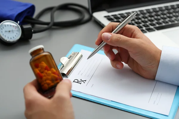 Hombre médico de la mano sostiene frasco de píldoras y escribir prescripciones — Foto de Stock
