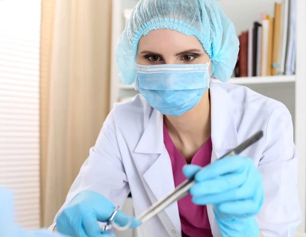 Bela cirurgiã feminina em máscara segurar agulha, pinça e pinça — Fotografia de Stock