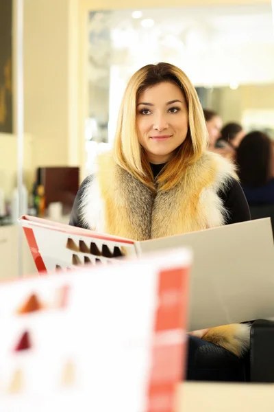 Beautiful blonde woman at hairdresser choosing new proper hairdo