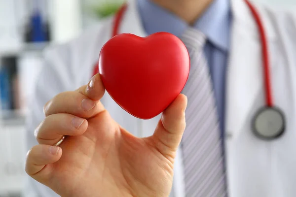 Médico masculino manos sosteniendo y cubriendo corazón de juguete rojo — Foto de Stock