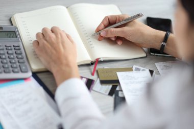 Kadın eli kalemi banka kartı ve hesap makinesinin yanında günlüğün üzerinde tutuyor..