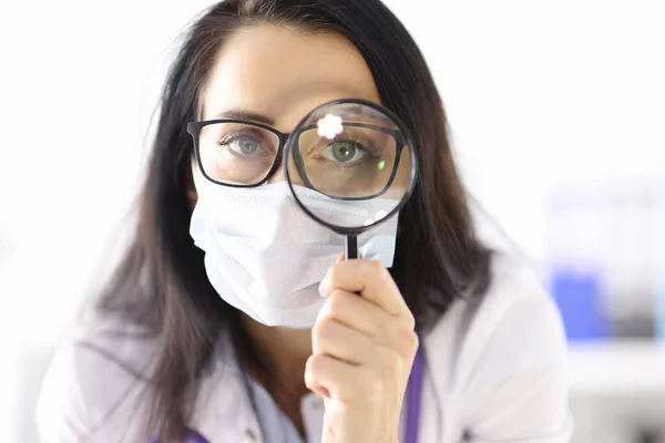 Doutor em máscara médica protetora olha através de lupa — Fotografia de Stock