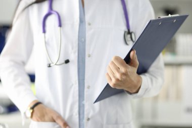Beyaz önlüklü doktor klinikte belgeli pano tutuyor.