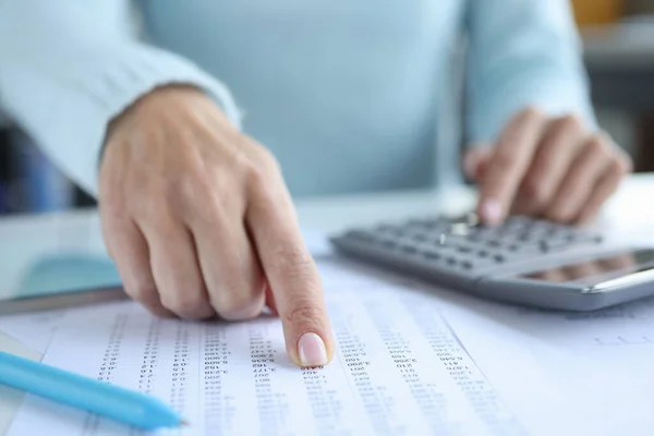 Vrouw wijst met haar vinger naar een document met cijfers en rekent op een close-up van de rekenmachine — Stockfoto