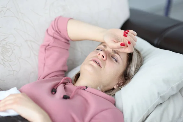 Mulher cansada deita-se no sofá com os olhos fechados e segura a mão na testa. — Fotografia de Stock