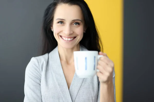 Mujer sonriente sosteniendo taza blanca en sus manos. — Foto de Stock