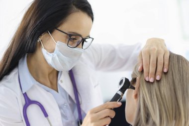 Otorhinolingolog klinikte otoskopla kadın hastaların kulaklarına bakıyor.