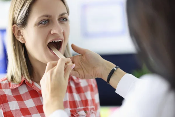 Dokter kijkend naar keel van vrouw patiënt met houten spatel in kliniek — Stockfoto