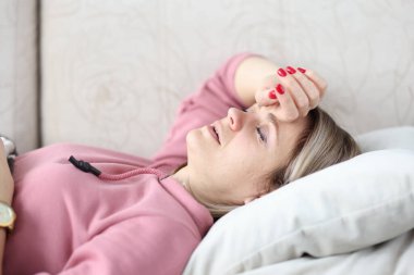 Hasta kadın kanepeye uzanmış, gözleri kapalı ve başını tutuyor.