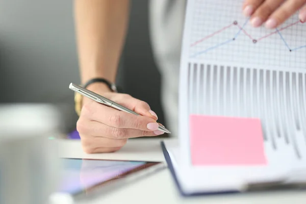 Kvinna skriva med kulspetspenna i dokument med grafer och diagram vid bordet i kontor närbild — Stockfoto