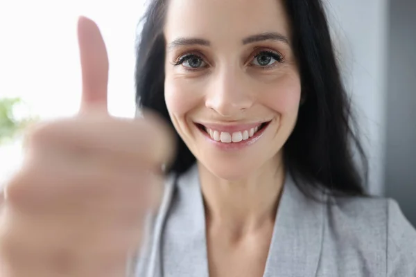 Улыбающаяся брюнетка-бизнесвумен, показывающая большой палец в офисе — стоковое фото