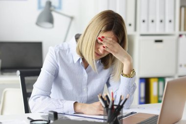 İş kadını ofiste oturuyor ve kafasını tutuyor.