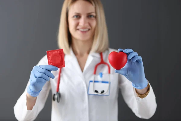 Doctor holds condom and red heart in his hand. — Stock Photo, Image