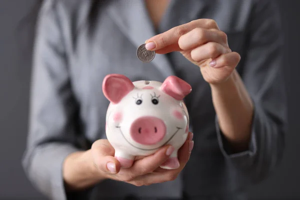 Female hand holds piggy bank and throws coin into it. — Stock Photo, Image