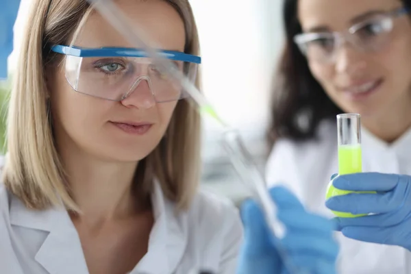 Cientistas femininas derramando líquido químico da pipeta em tubo de ensaio em laboratório — Fotografia de Stock