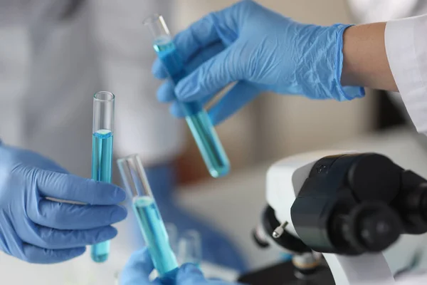 Hände in Gummihandschuhen halten im Reagenzglas mit blauer Flüssigkeit im Labor — Stockfoto
