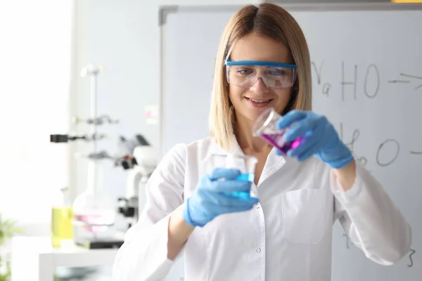 Mujer científica en gafas de seguridad vertiendo solución química del matraz en laboratorio — Foto de Stock