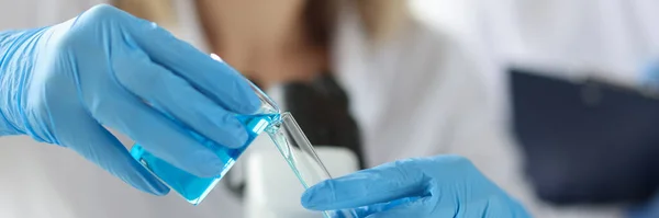 Mani di scienziato in guanti versando liquido blu nella provetta — Foto Stock