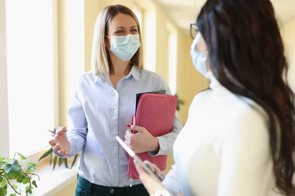 Tıbbi koruyucu maskeli iki iş kadını ofiste konuşuyor.. — Stok fotoğraf