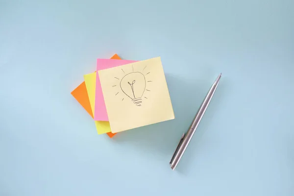 La bombilla está dibujando en un pedazo de papel. Muchas pegatinas de colores y bolígrafo acostado en la mesa —  Fotos de Stock