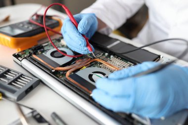 Profesyonel tamirci dizüstü bilgisayarın üzerinde kırmızı eldivenli test cihazı tutuyor.