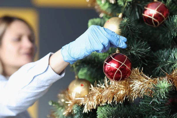 Frau in schützenden Gummihandschuhen hängt Ball in Großaufnahme am Weihnachtsbaum — Stockfoto