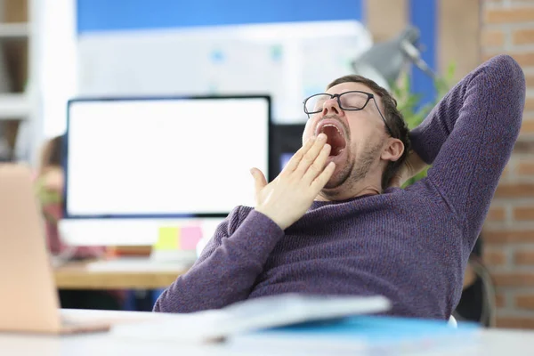 Young man siting at table in office and yawning — Stock Photo, Image