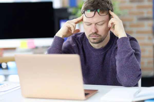 Hombre sentado en frente de la computadora portátil y sosteniendo su cabeza — Foto de Stock
