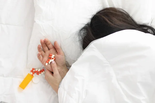 Kvinnors hand sticker ut under täcket, piller ligger på hennes hand. — Stockfoto