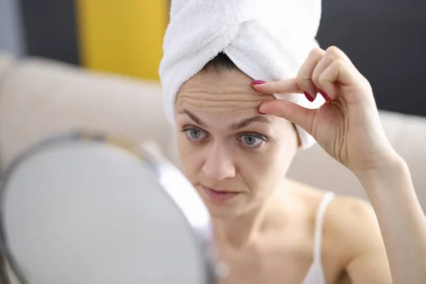 Kobieta bada zmarszczki na czole w lustrze — Zdjęcie stockowe
