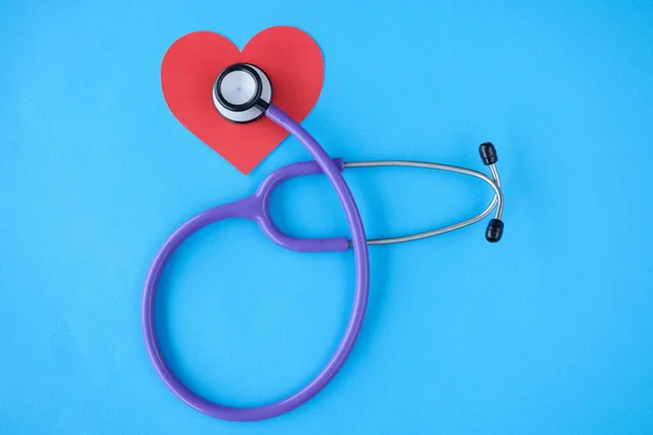 Stethoscope lying on red paper heart on blue background