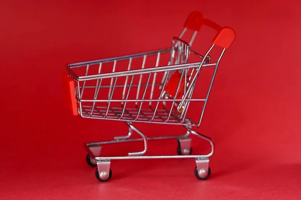 Мініатюрний іграшковий продуктовий візок, що стоїть на червоному тлі — стокове фото
