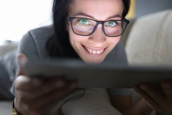 Mulher sorridente com óculos encontra-se no sofá e segura tablet — Fotografia de Stock