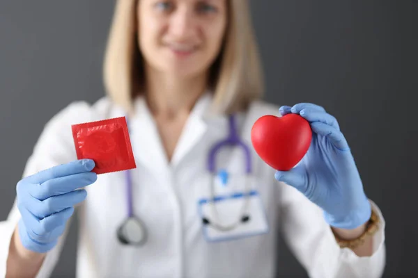 Doktorn håller kondom och hjärta i handen — Stockfoto