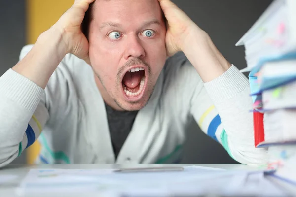 Dumbfounded man holds his head and looks at the stack of folders — Stock Photo, Image