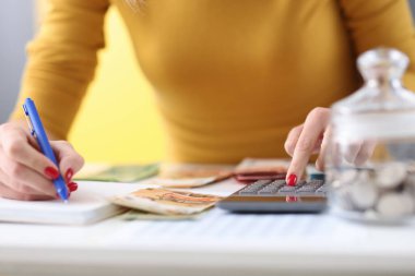 Kadınların elleri kalem tutuyor ve hesap makinesinde banknotları sayıyorlar.
