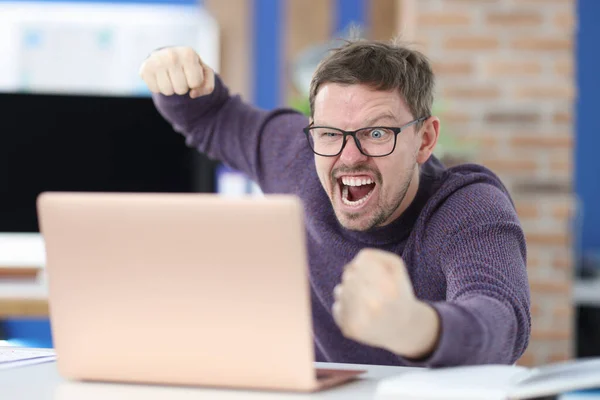 Uomo arrabbiato con gli occhiali ondeggia il pugno al monitor del computer portatile — Foto Stock